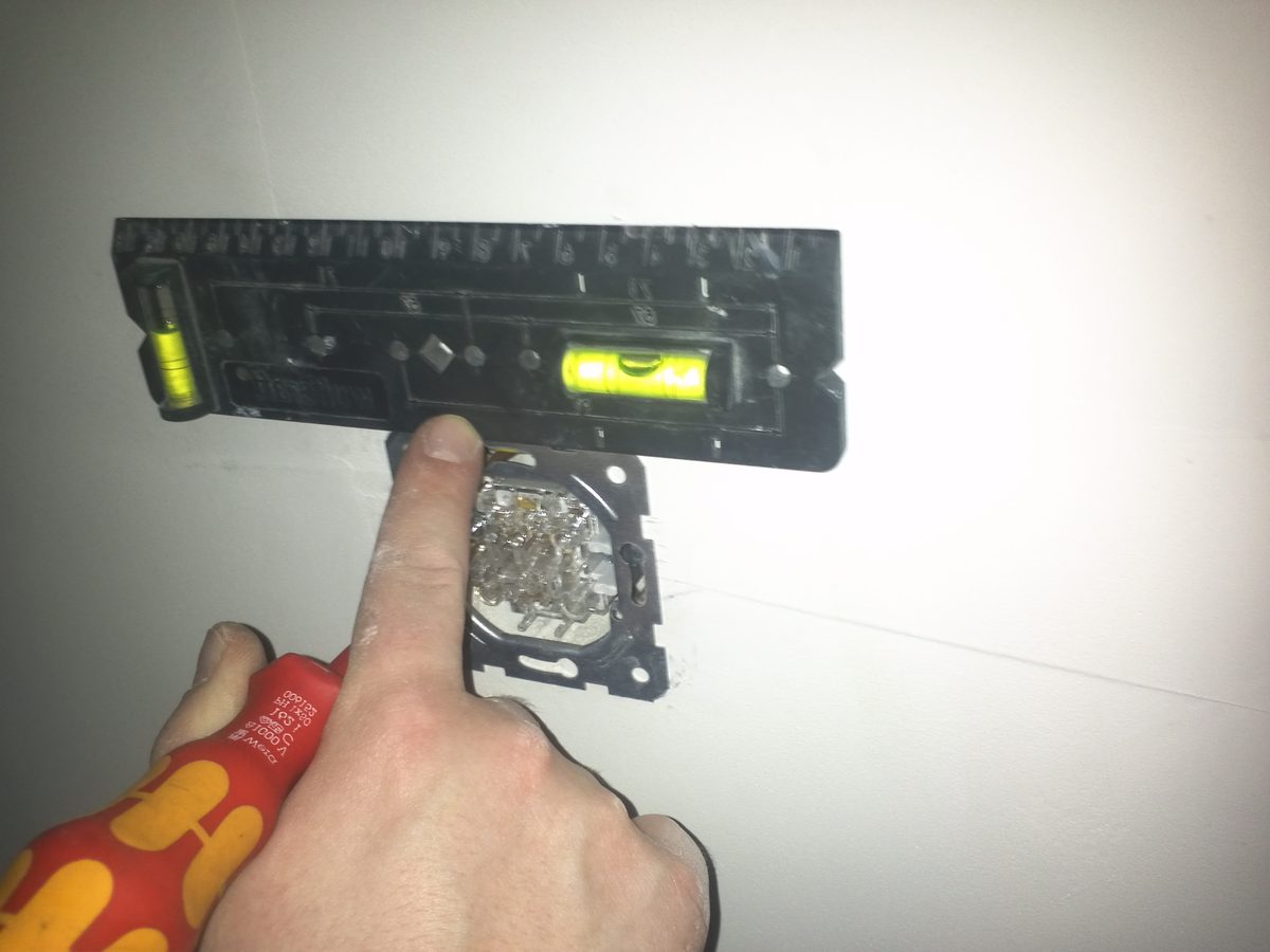Ręka z wkrętakiem izolowanym VDE montująca łącznik w puszce elektrycznej
